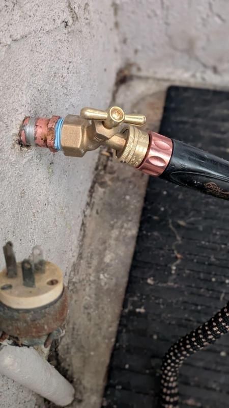 A close up of a hose attached to a faucet on a wall.