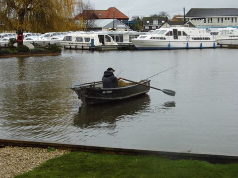 Solitary fisherman in fishing rowing boat on river Bure