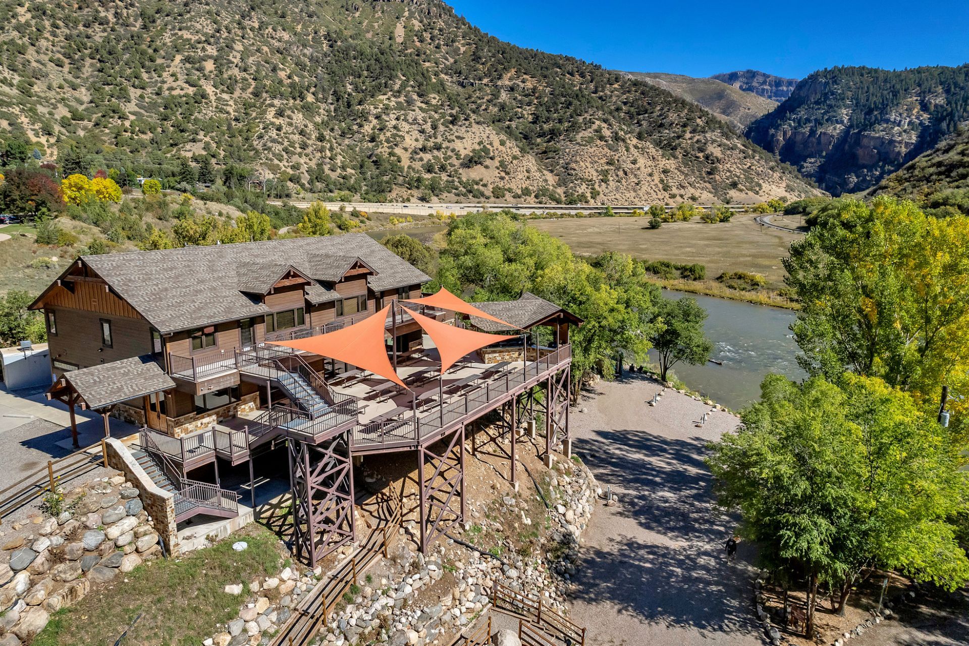 An aerial view of a large house surrounded by trees and mountains next to a river.