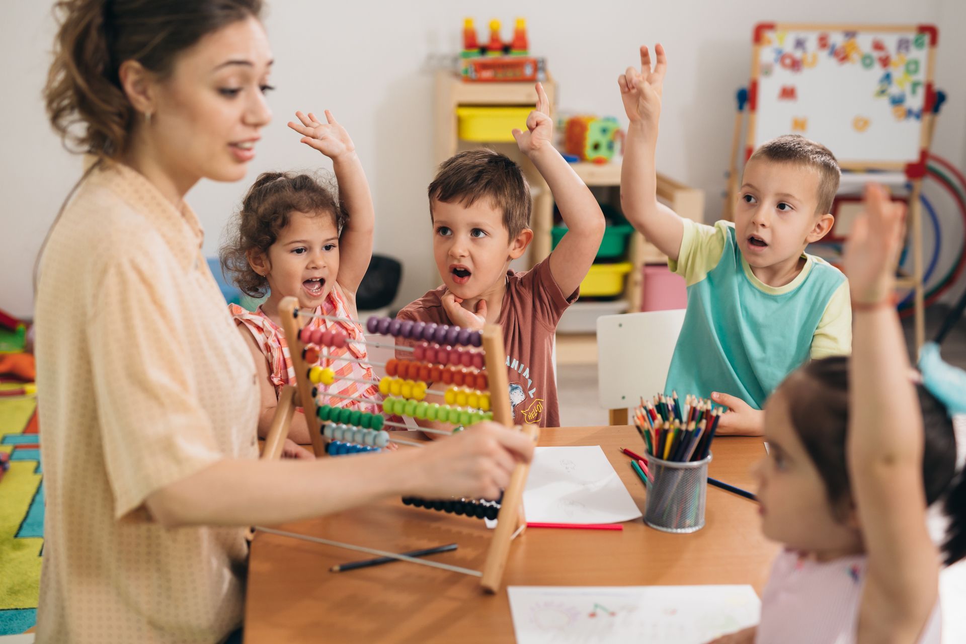 An educator with an abacus with four kids holding up their hands at a kindergarten table.