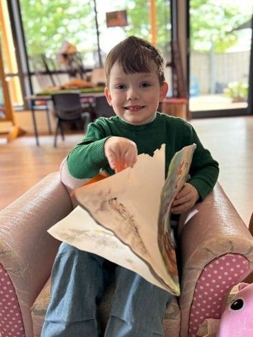 Young child in green shirt and blue pants reading a book while seated in a small armchair. Young child in green shirt and blue pants reading a book while seated in a small armchair.