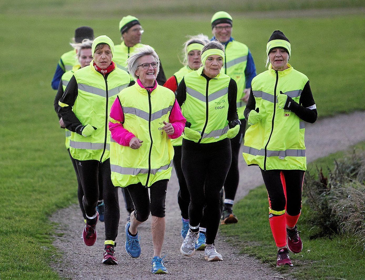 En gruppe mennesker iført neongule veste løber på en sti.