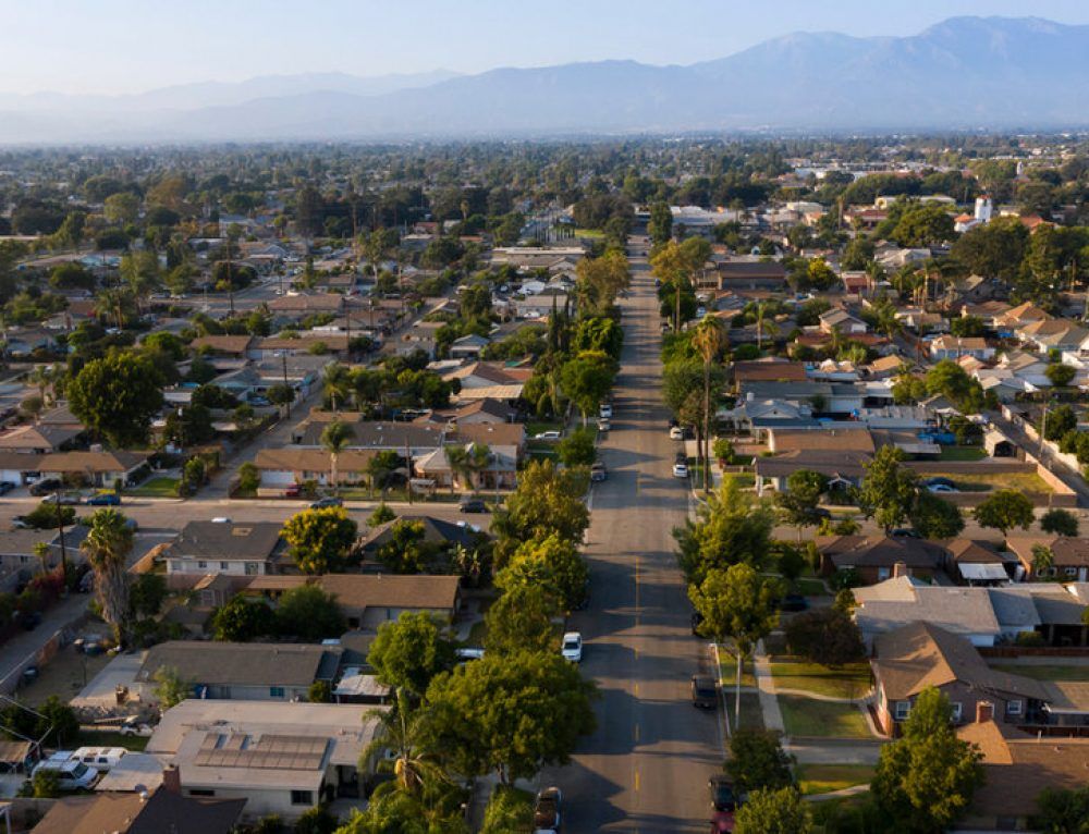 Aerial view of a suburban neighborhood with houses and trees lining streets, mountains in the background.