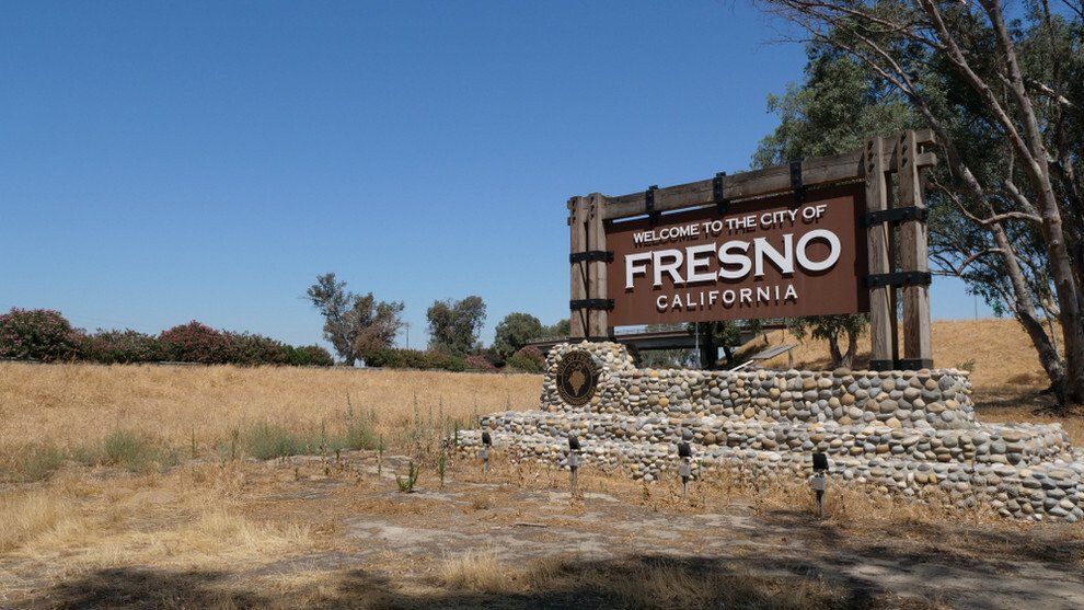 Welcome sign to Fresno, California, in a field of dry grass under a clear blue sky.