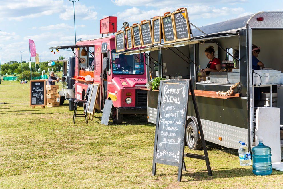 A row of food trucks are parked in a field.