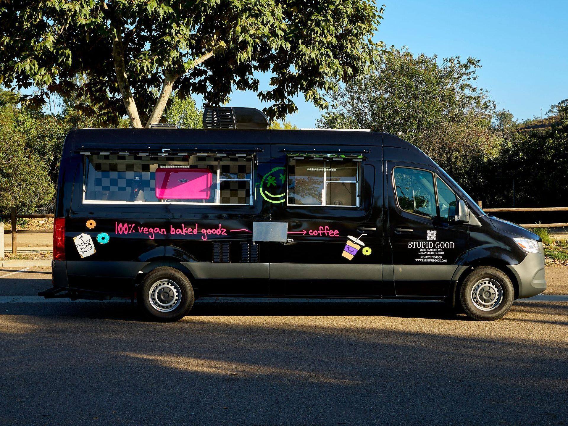 Black food truck with bright graphics, parked outdoors under trees.