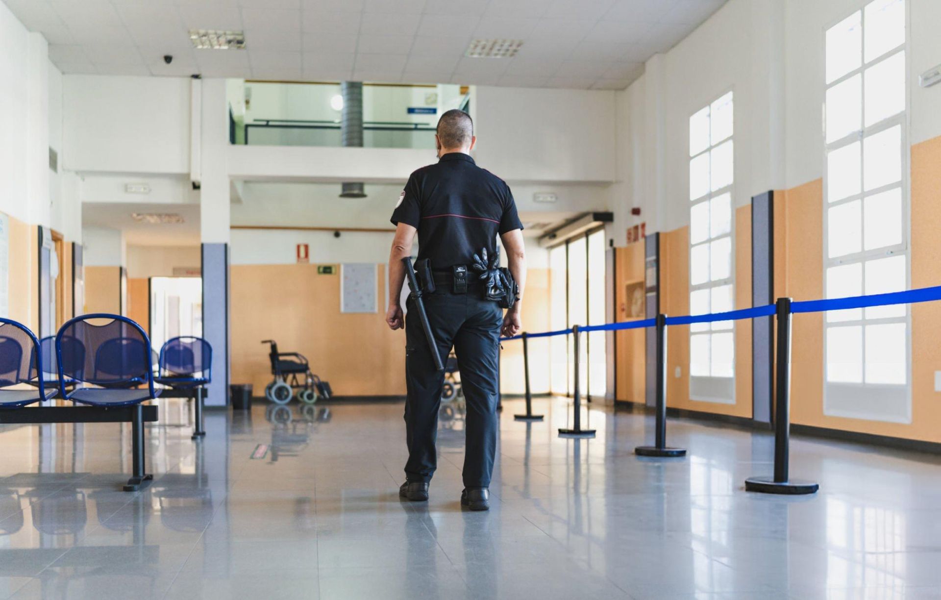 Security guard walking in a hospital corridor with blue chairs and wheelchair. Security guard walking in a hospital corridor with blue chairs and wheelchair.