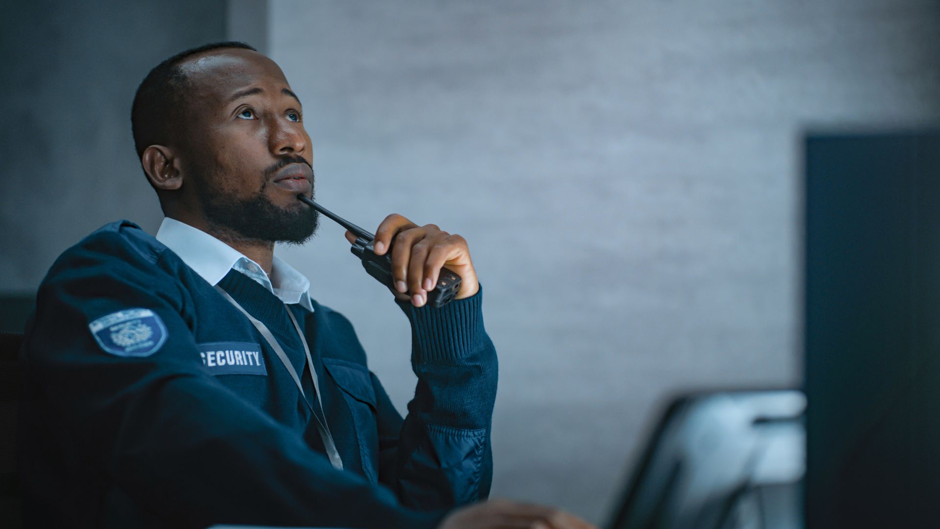 African American security officer with a walkie talkie in monitoring center at night.