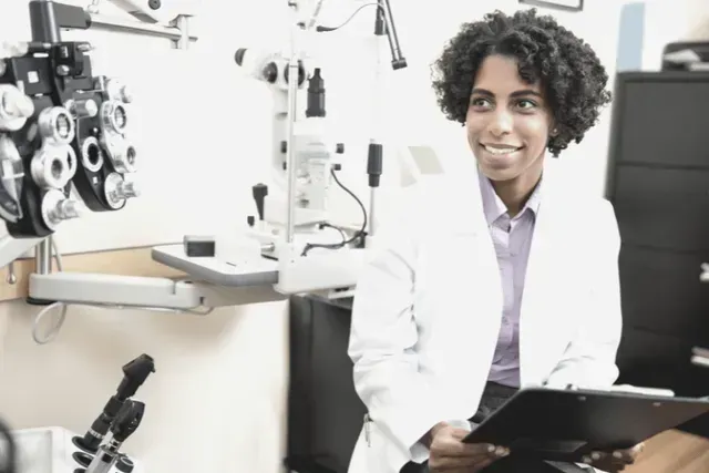 A woman in a lab coat is holding a clipboard in an office.