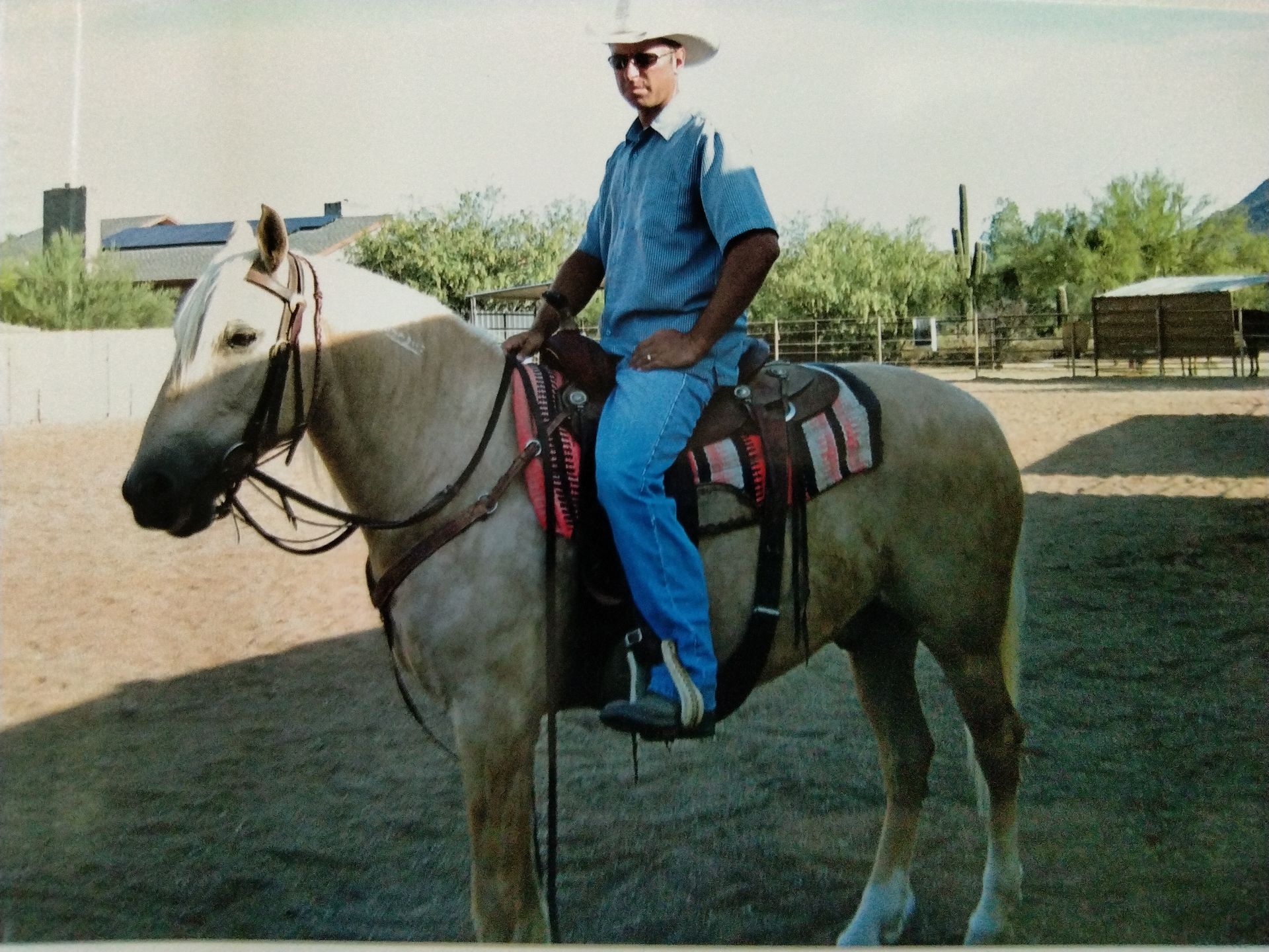 Man in a cowboy hat sits on a palomino horse, outside.