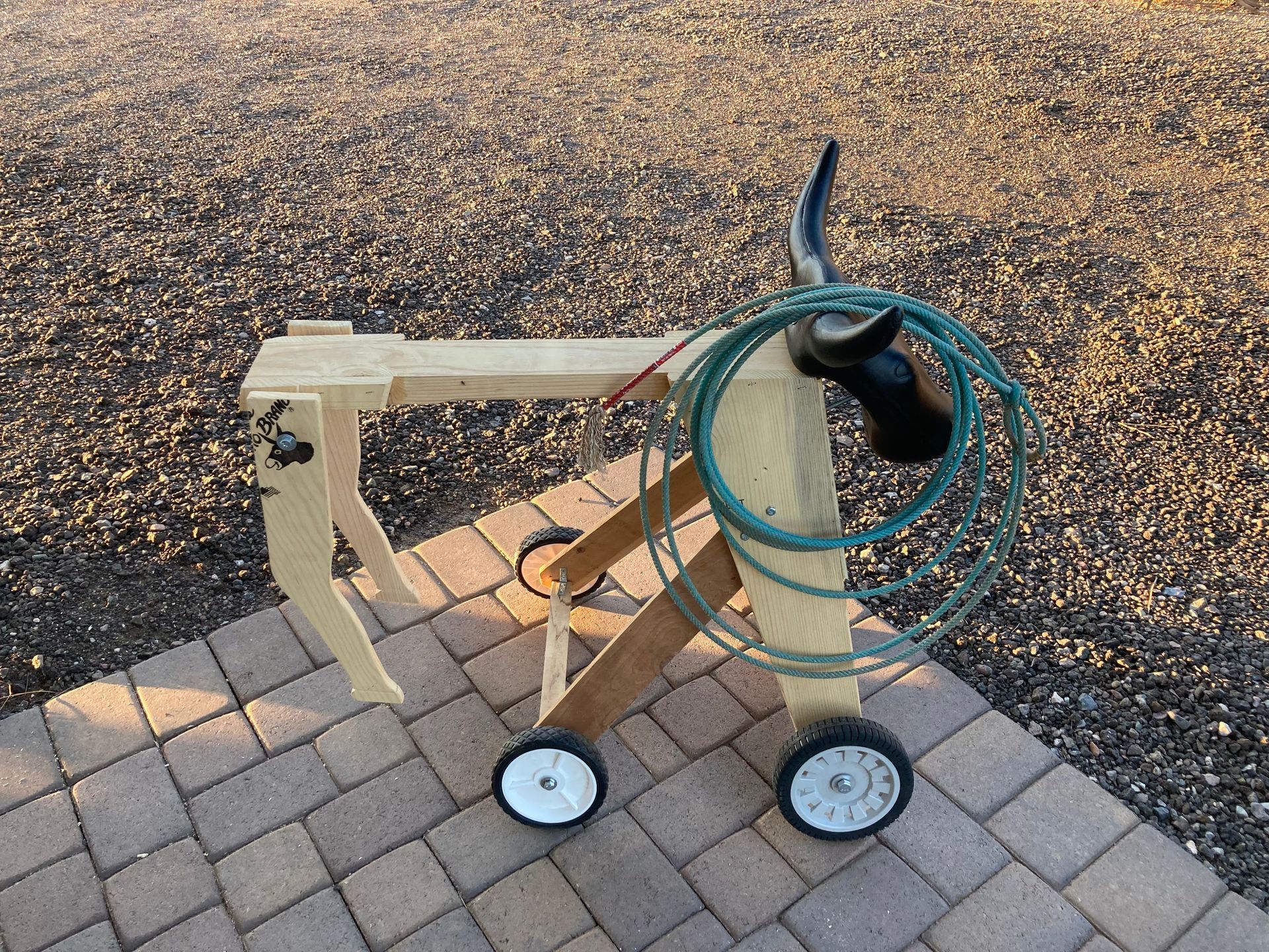 Wooden hose cart with bull head, coiled green hose, and a wood sawhorse on a brick patio. roping dummies