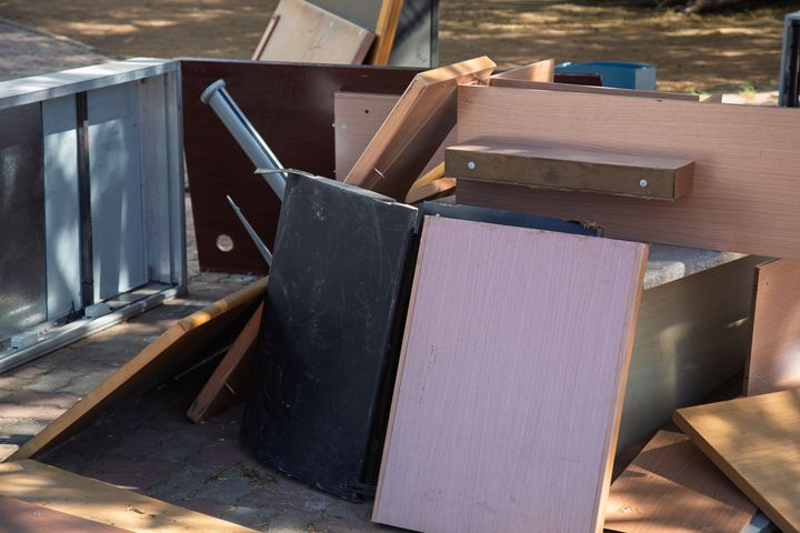 A pile of discarded wooden and metal furniture scraps on a paved surface.