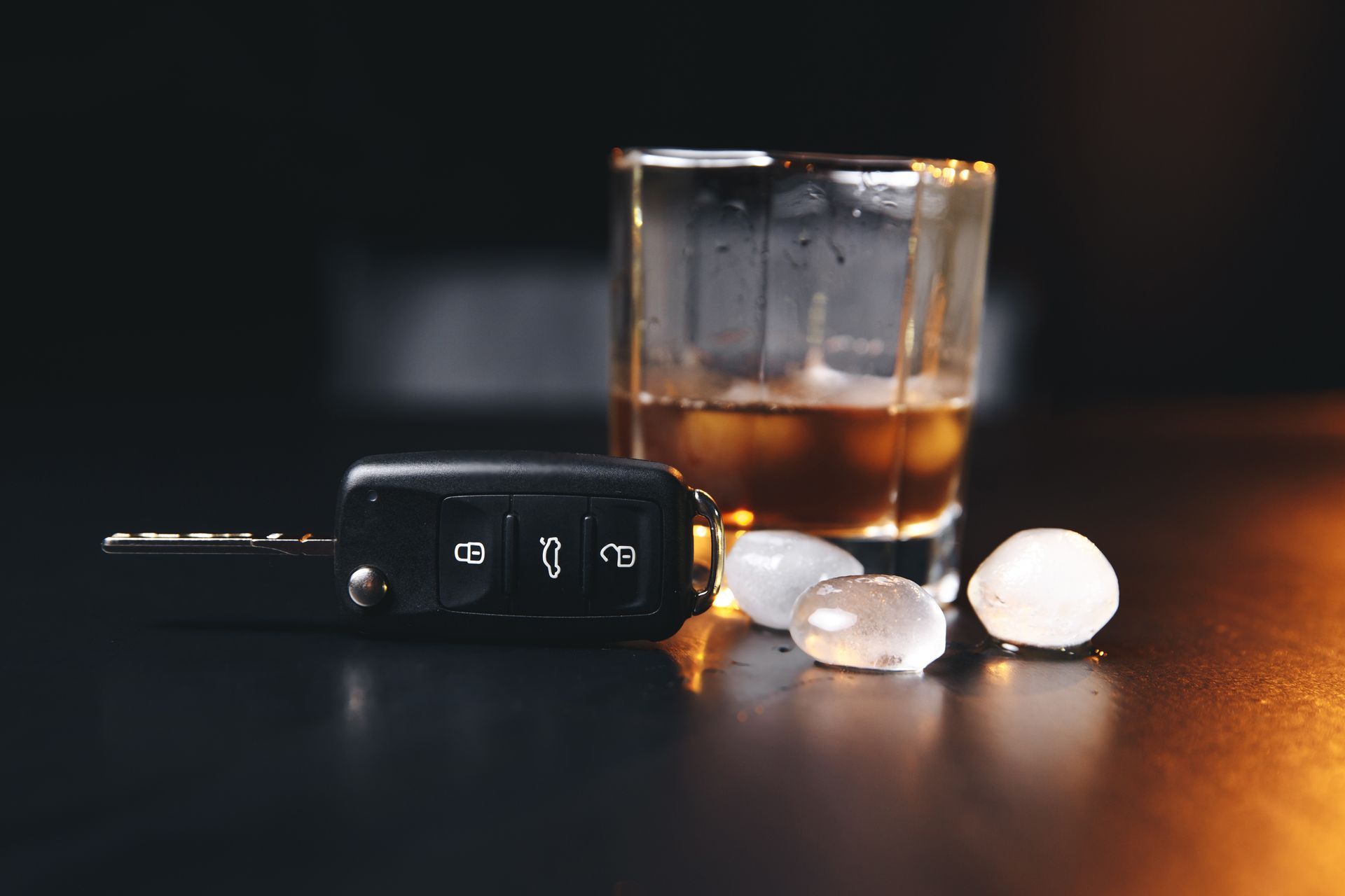 Car keys next to a shot of whiskey on a table, implying drunk driving.