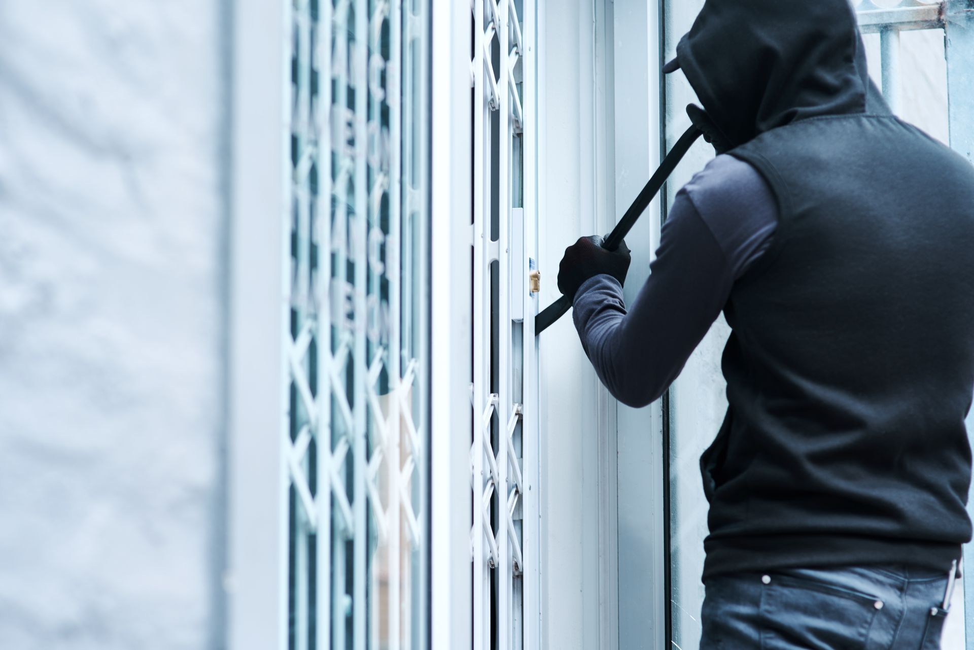A man in a mask is breaking into a door with a crowbar.