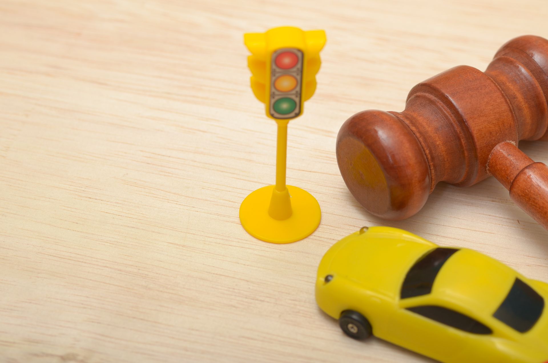Toy car and traffic light next to a wooden gavel on a light wood surface.