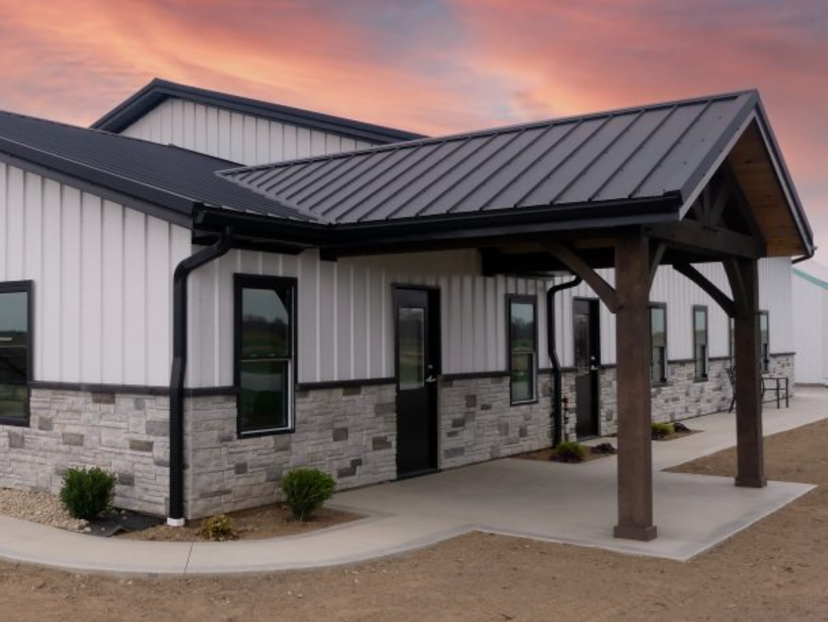 Modern white building with black roof and trim, stone accents, and a covered entryway under an orange sky.