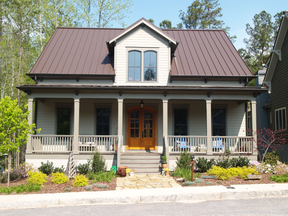 Tan house with brown metal roof, front porch, and small landscaping.