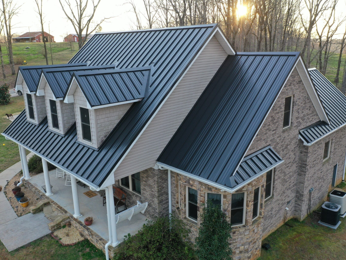 Dark metal roof on a two-story brick house with dormers and a porch.