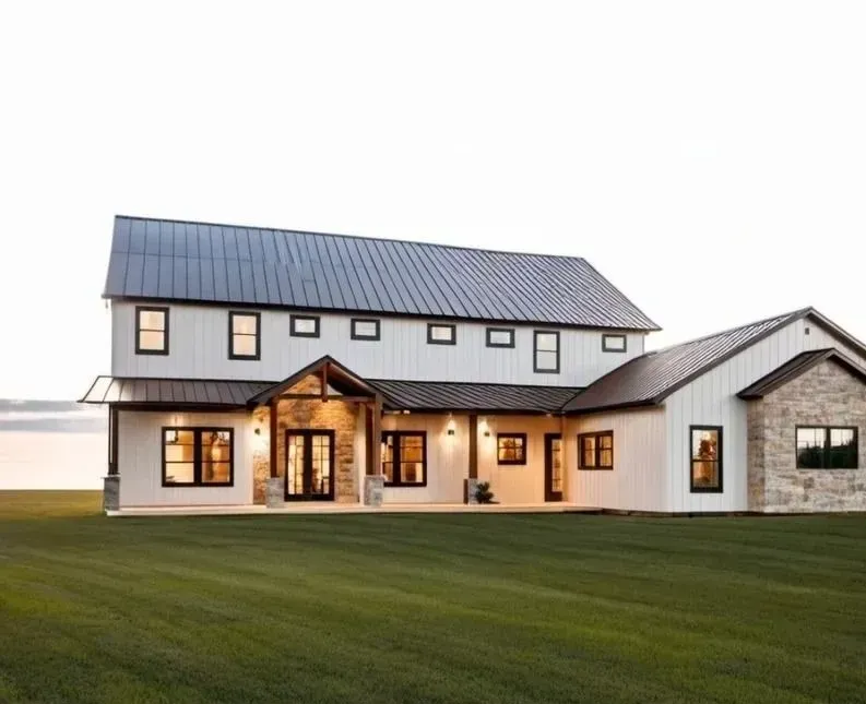 Two-story modern farmhouse with white siding, black trim, and a metal roof against a grassy field.
