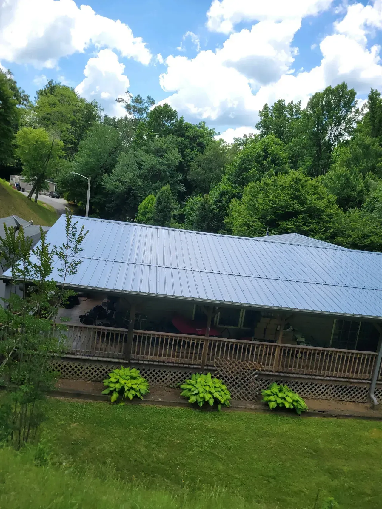 Cabin with a metal roof and porch, surrounded by green trees under a cloudy blue sky.