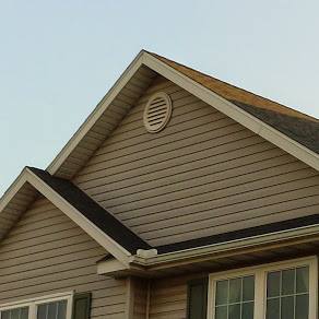 A beige, vinyl-sided house exterior showing two gabled roof peaks and a circular vent under the main roof peak.