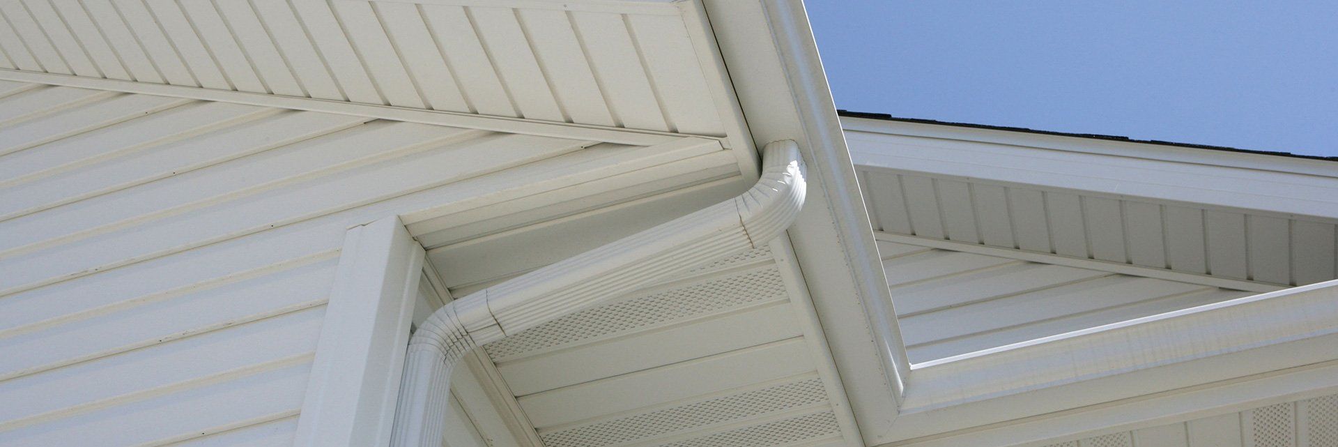 White vinyl siding and soffits on the exterior corner of a house under a blue sky.