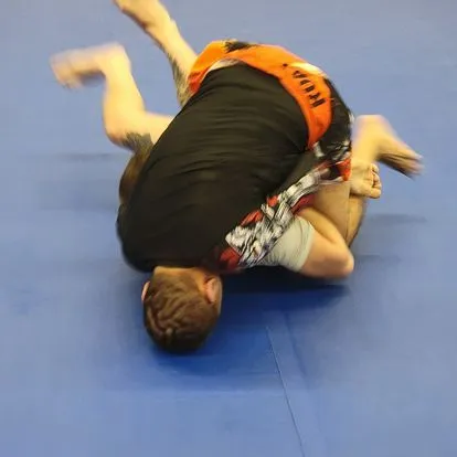 A man in a black shirt and orange shorts is laying on his back on a blue mat.