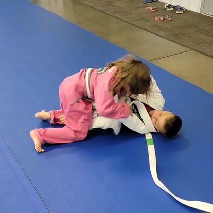 A boy and a girl are wrestling on a blue mat