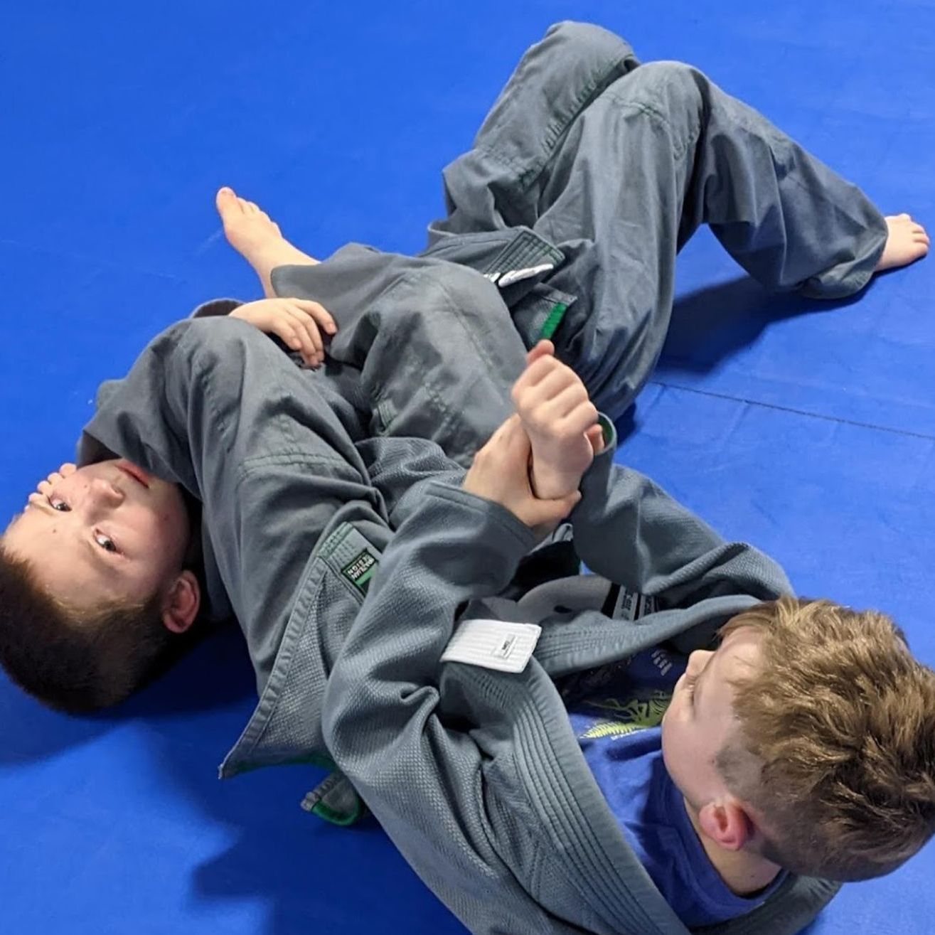 Two boys are wrestling on a blue mat