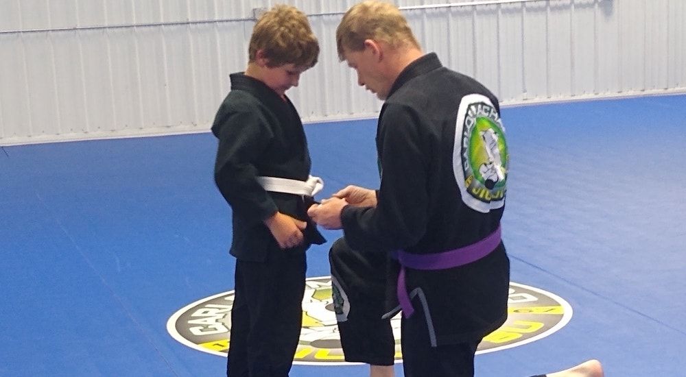 A man is helping a young boy with his karate belt
