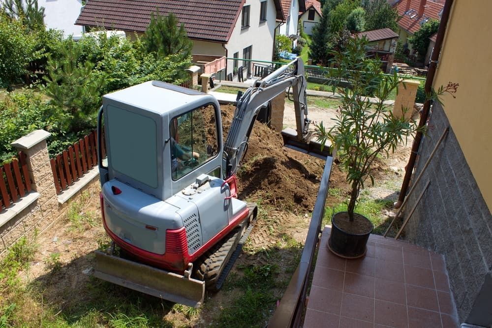 A Small Excavator Is Digging A Hole In The Ground In Front Of A House - Micro Excavations & Earthmoving in Burleigh Heads, QLD