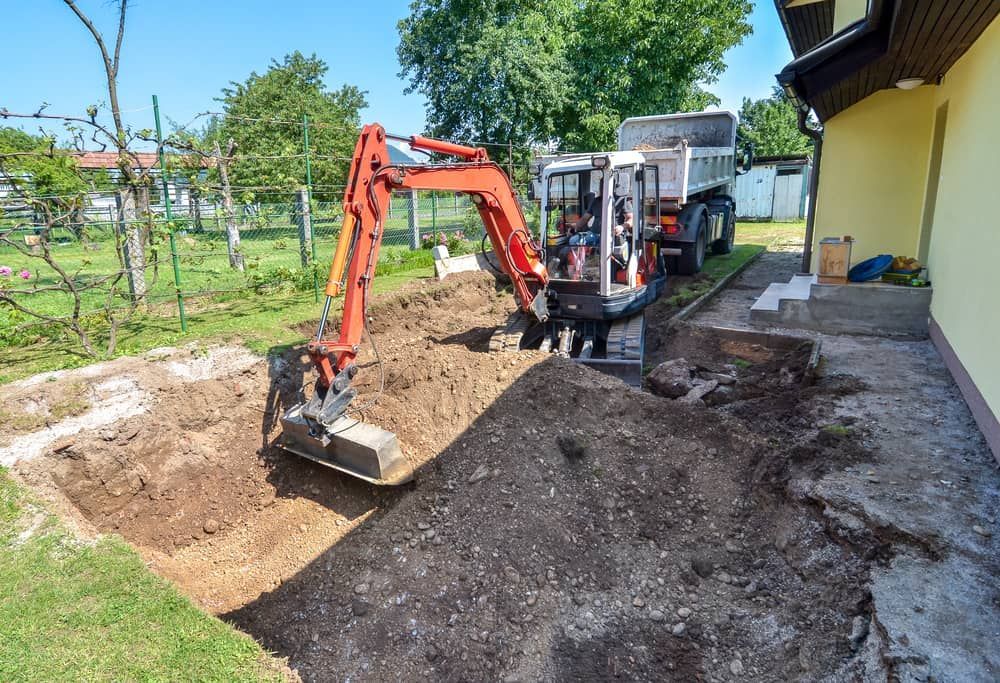 An Excavator Is Digging A Hole In The Ground In Front Of A House - Micro Excavations & Earthmoving in Burleigh Heads, QLD