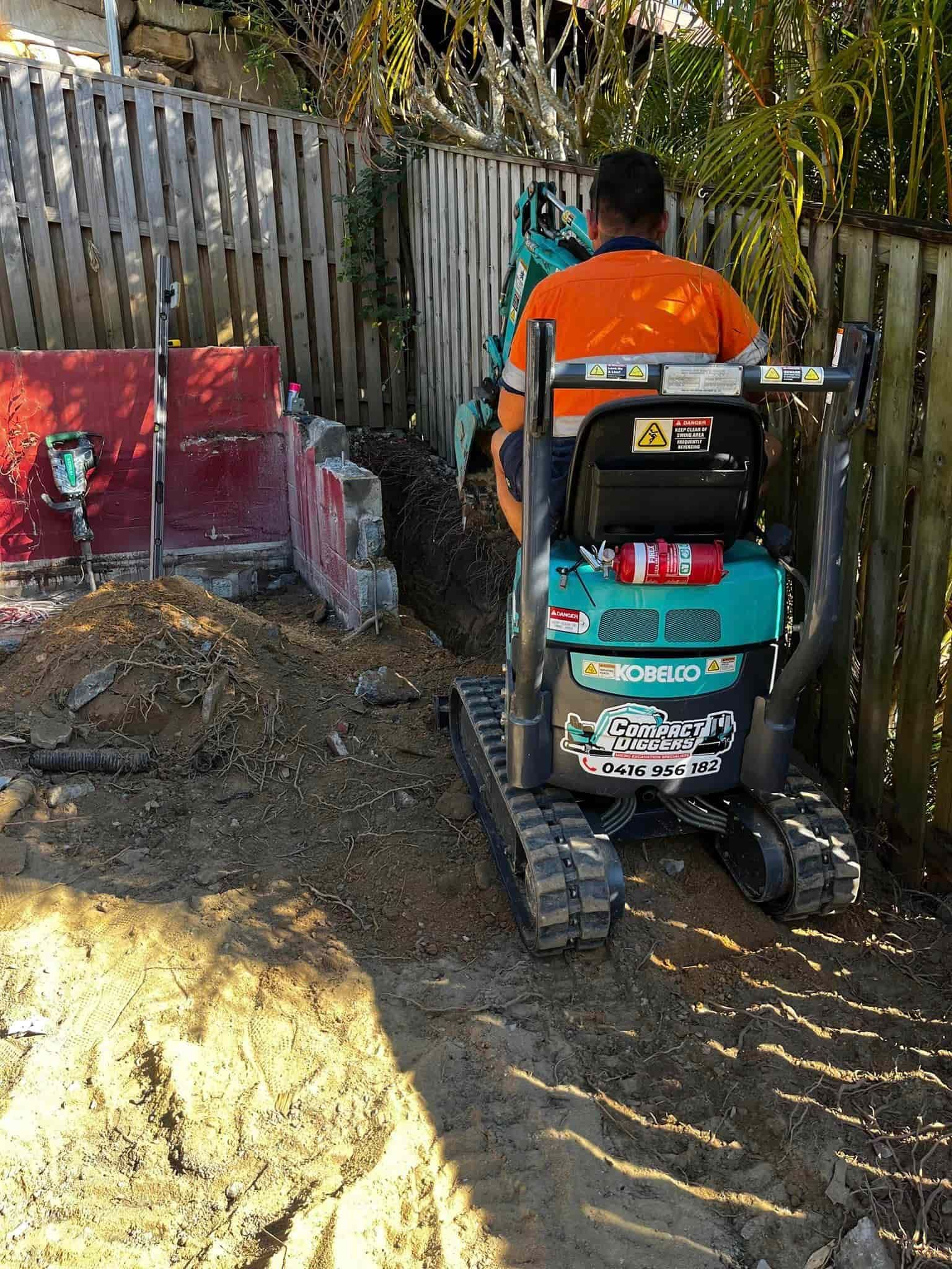 A Man Is Driving A Compact Excavator - Mini Earth Works & Excavation on the Gold Coast, QLD