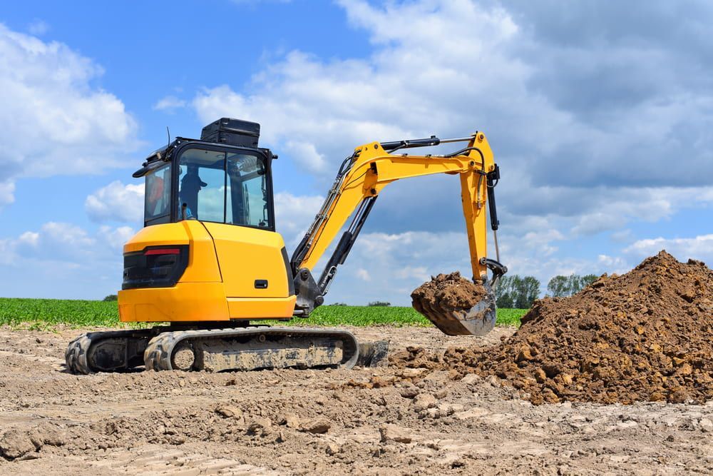 A Yellow Excavator Is Digging A Pile Of Dirt In A Field - Micro Excavations & Earthmoving in Southport, QLD