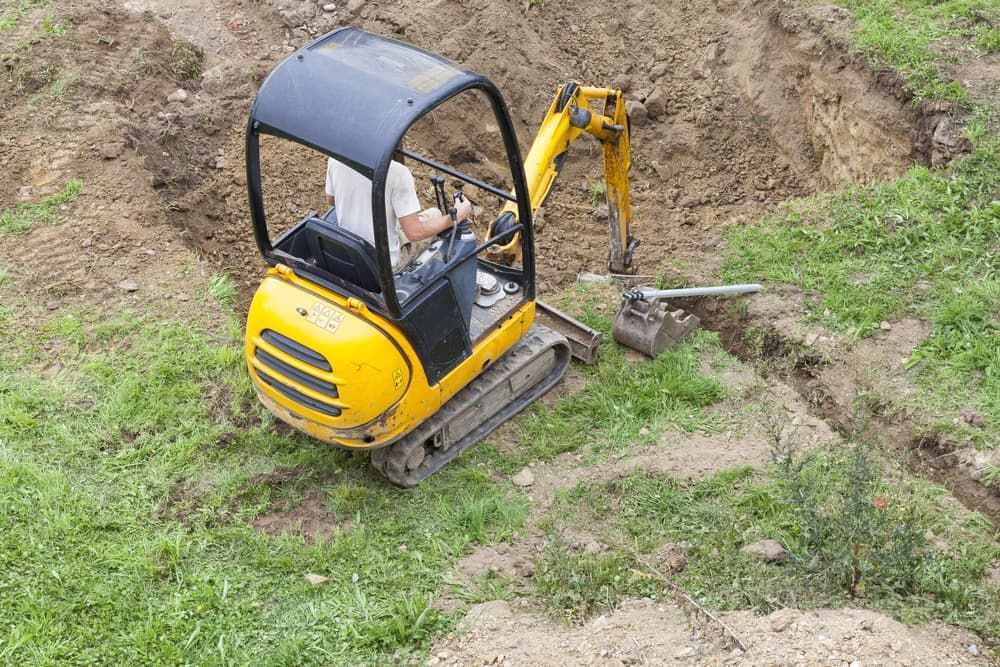 A Man Is Driving A Small Yellow Excavator In A Dirt Field - Micro Excavations & Earthmoving in Nerang, QLD