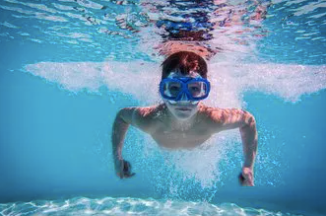 Picture of a little boy wearing blue goggles swimming underwater. 