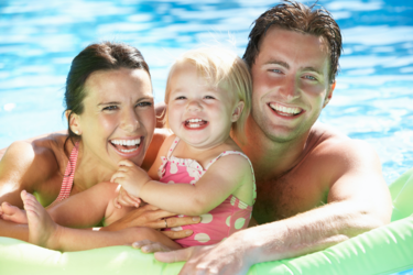 Picture of mom and dad holding little baby girl in pink swimsuit on green floaty in swimming pool.