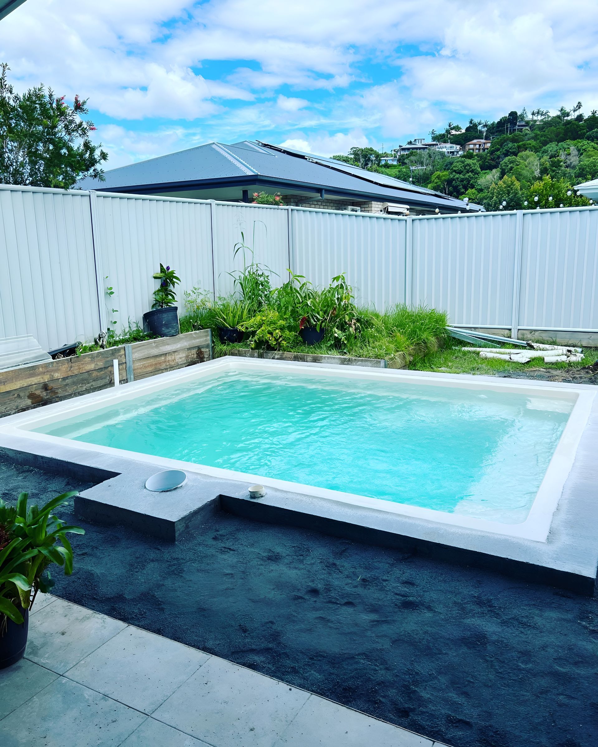 Small rectangular pool with turquoise water, surrounded by a white border and fence, set in a backyard.