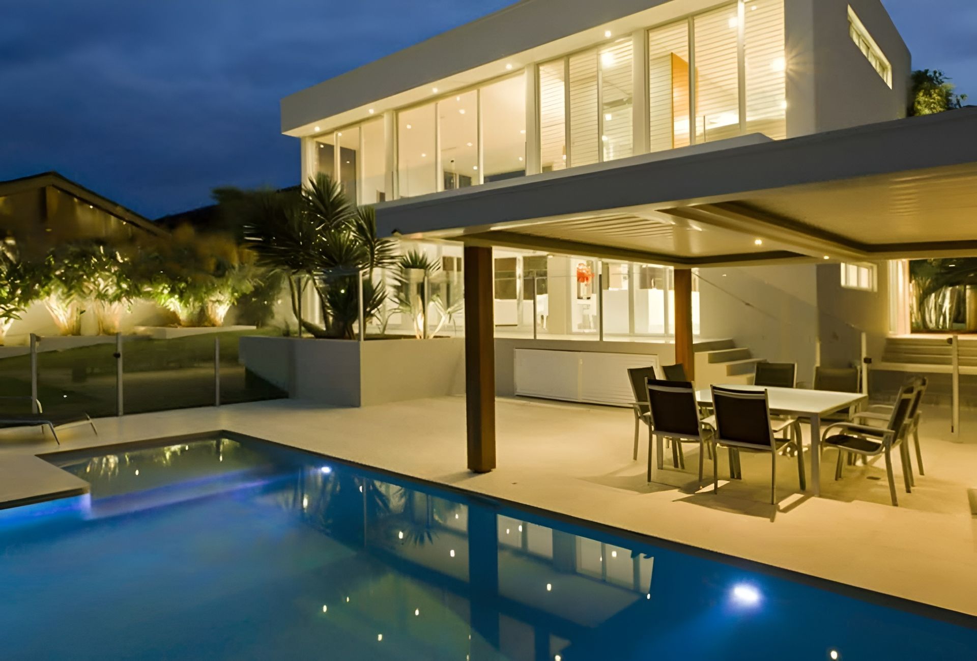 Modern White House With a Pool and Outdoor Dining Area Lit at Night — Bombs Away Pools in Southport, QLD