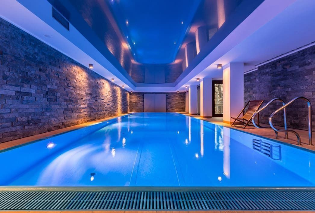 Indoor Pool With Blue Lighting, Stone Wall, and Lounge Chairs — Bombs Away Pools in Robina, QLD