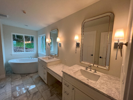 A bathroom with two sinks, a tub and two mirrors where Mauro Electric installed the lights and wiring.