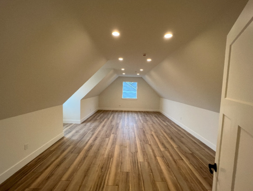An finished attic with hardwood floors and a window with electrical work done by Mauro Electric.