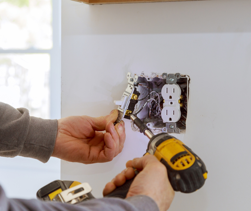 A man is installing an electrical outlet on a wall with a drill.