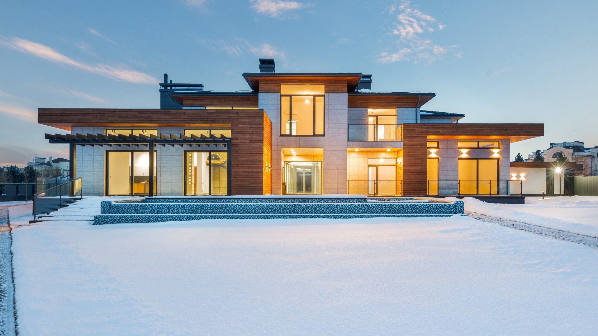 A large house with a lot of windows is sitting in the snow.
