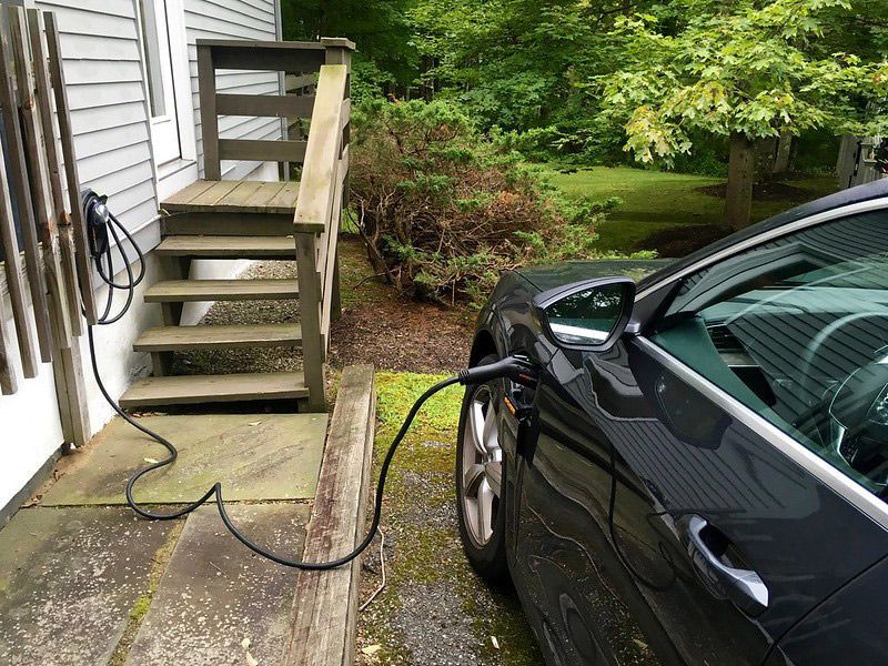 A car is being charged by a level 2 EV charging station outside of a house.