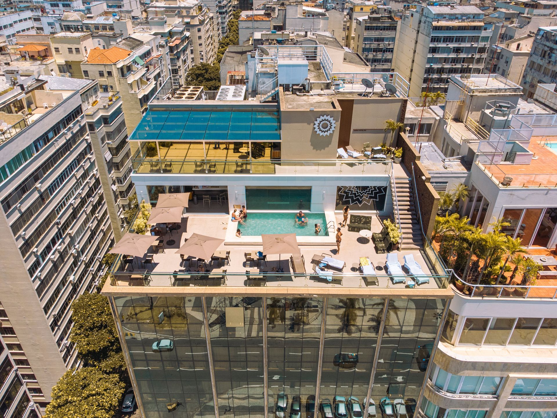 Um quarto de hotel com uma cama com um caminho de mesa de estampa tropical azul e amarela, uma TV fixada na parede e móveis de madeira.