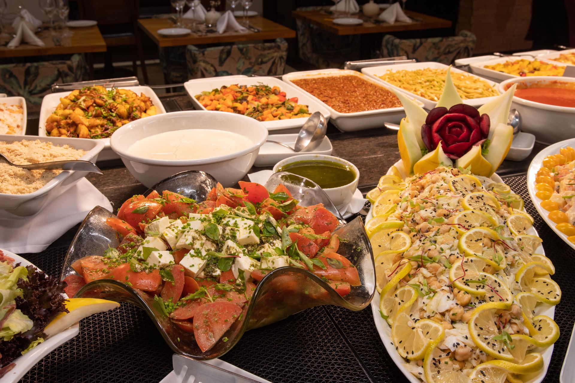 Uma mesa de bufê com tigelas de saladas, massas, rodelas de limão e pratos de legumes em um ambiente de restaurante.