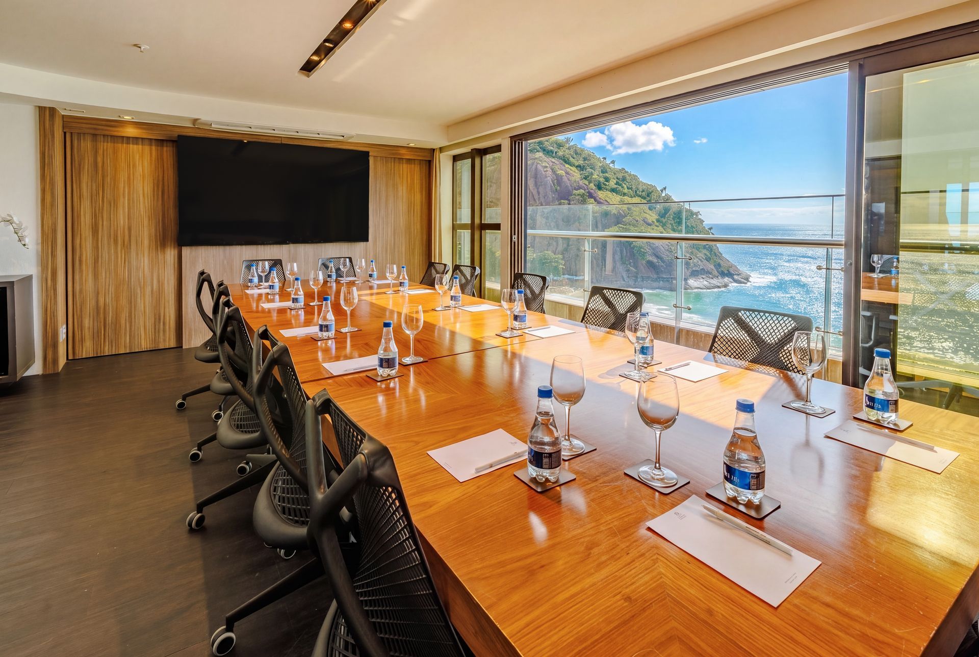 Sala de conferências moderna com fileiras de cadeiras voltadas para uma tela e janelas com vista para o mar.