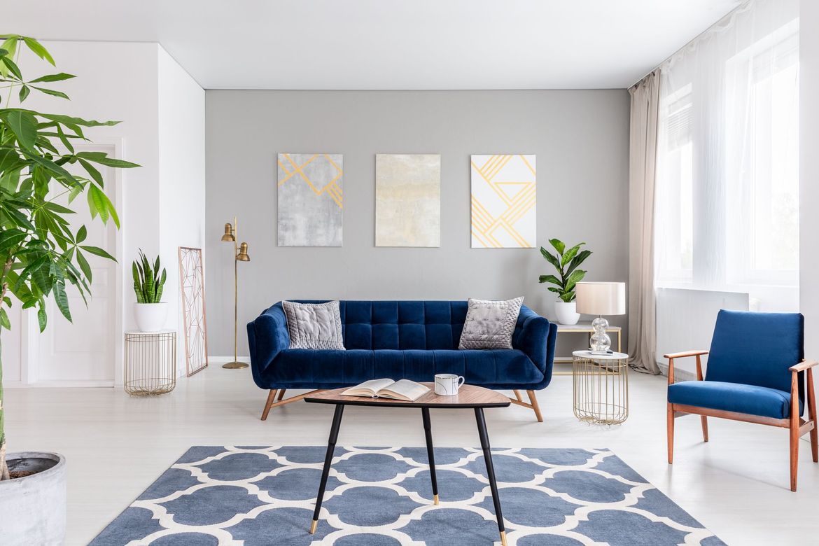 A living room with a blue couch , chairs , table and rug.