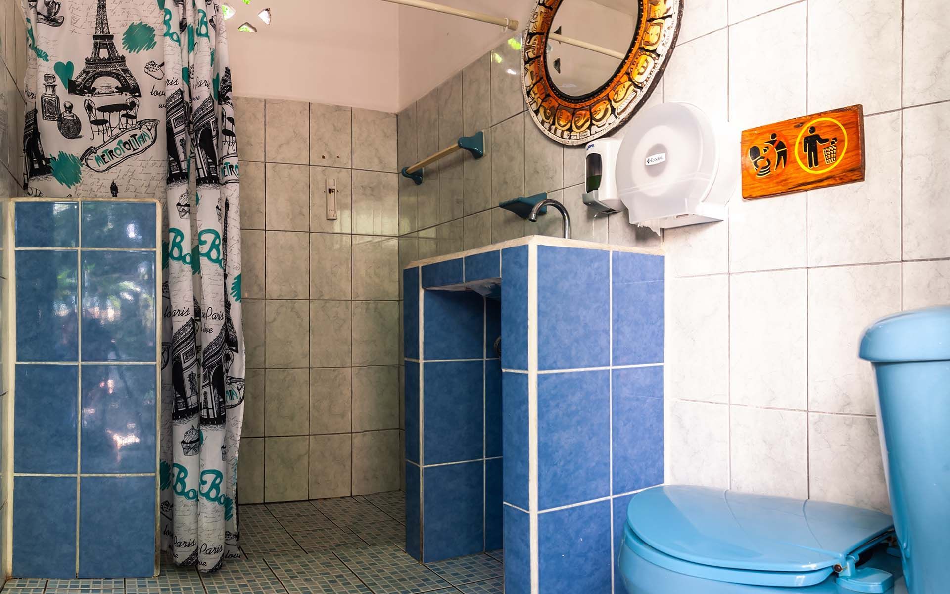 Baño con azulejos azules, lámparas, inodoro, lavabo y ducha con cortina de la Torre Eiffel.